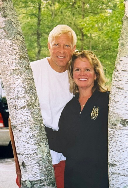 Smiling couple standing close together between two birch trees in a park.