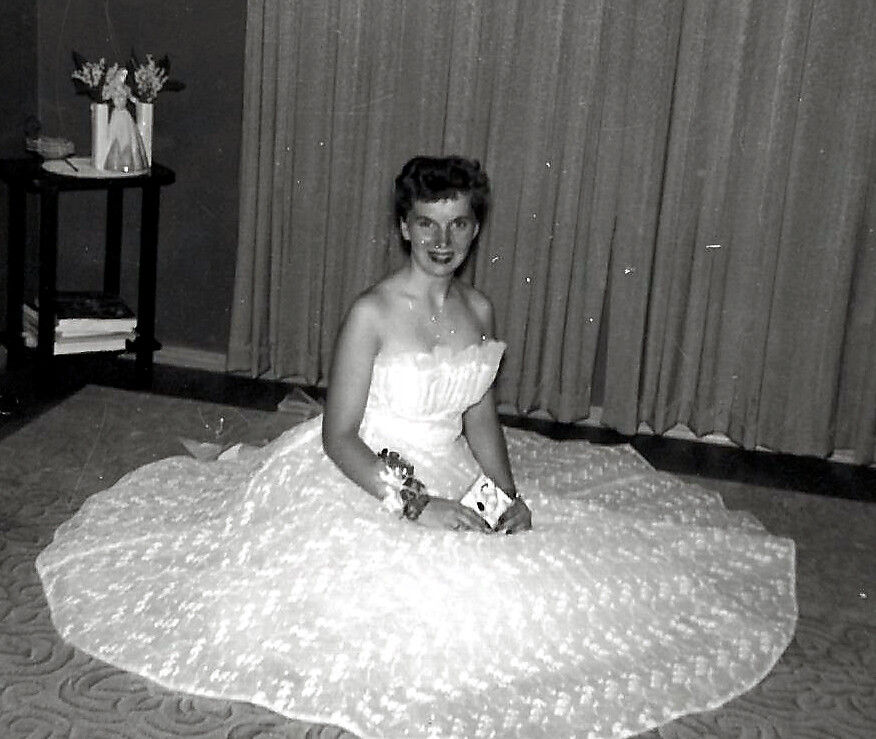 Bride in a vintage strapless wedding gown kneeling on a carpeted floor with a very full skirt spread around her.