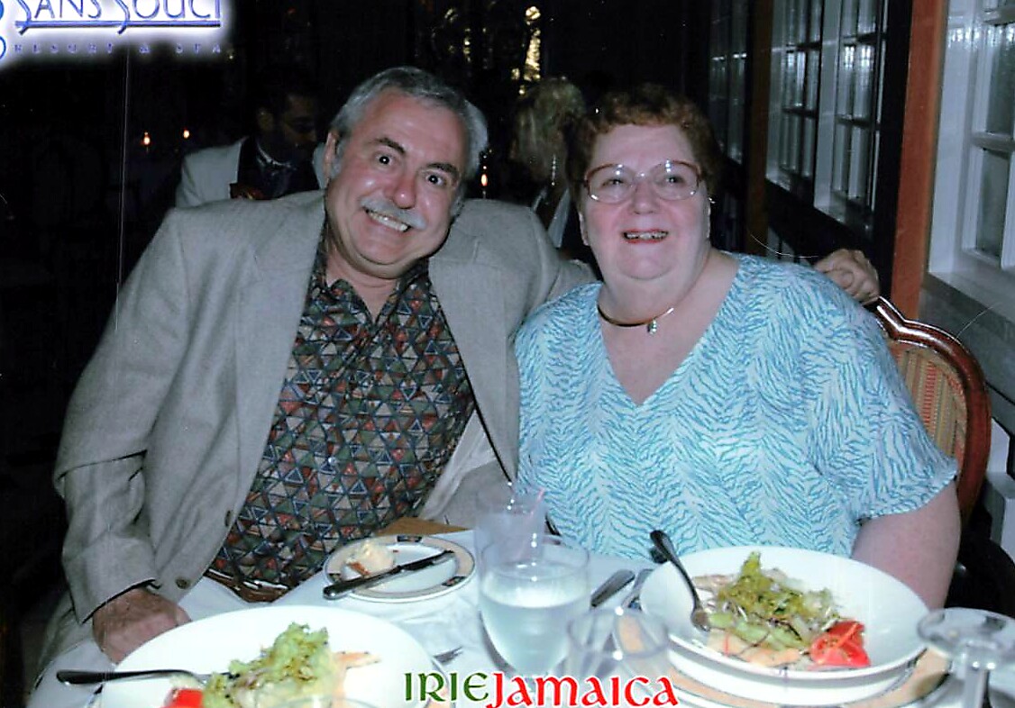 Smiling elderly couple seated at a restaurant table with salad plates in front; watermark 'IRIE Jamaica' across the bottom.
