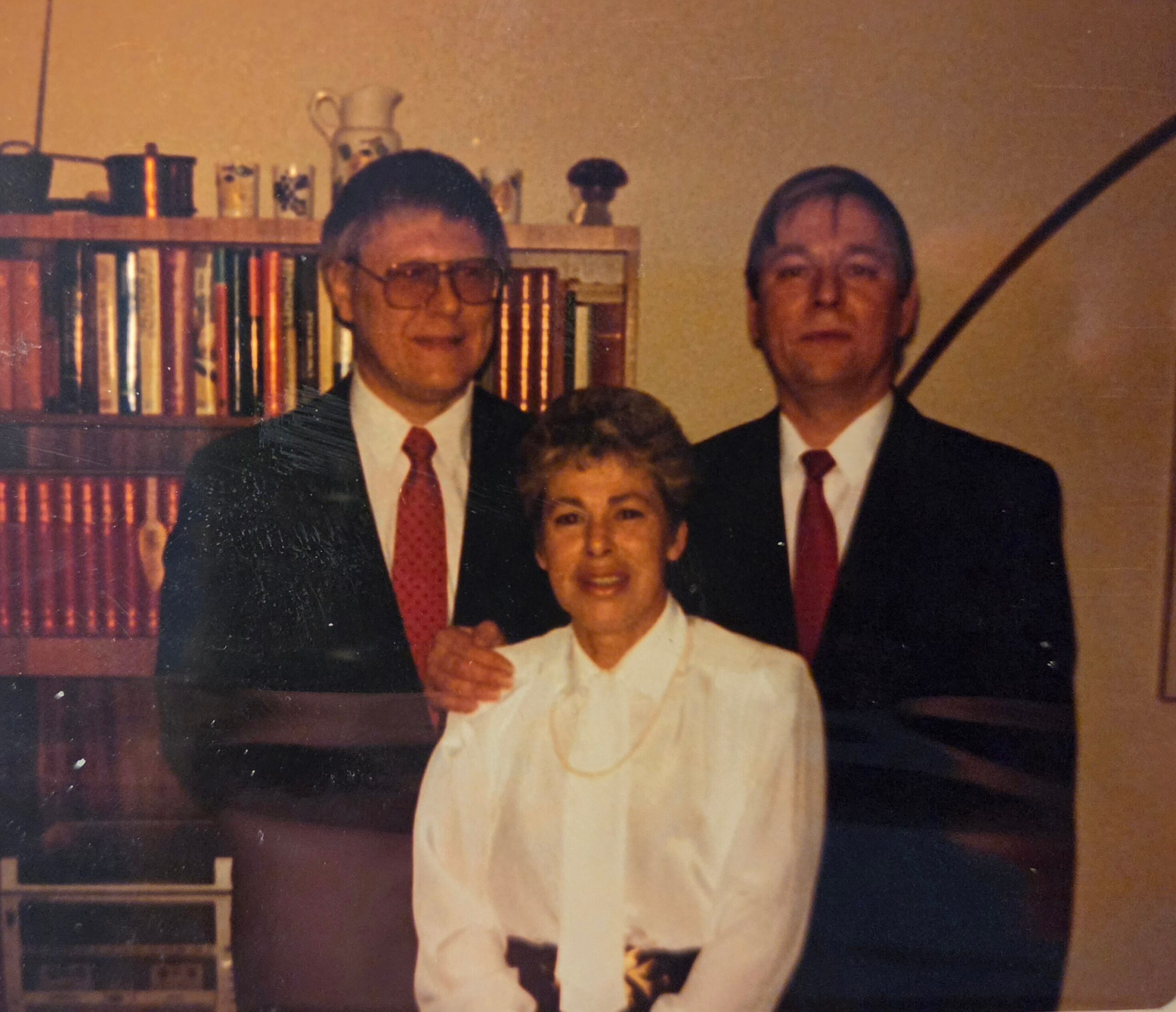 Family portrait: three adults in formal attire posing indoors, with a bookshelf in the background.