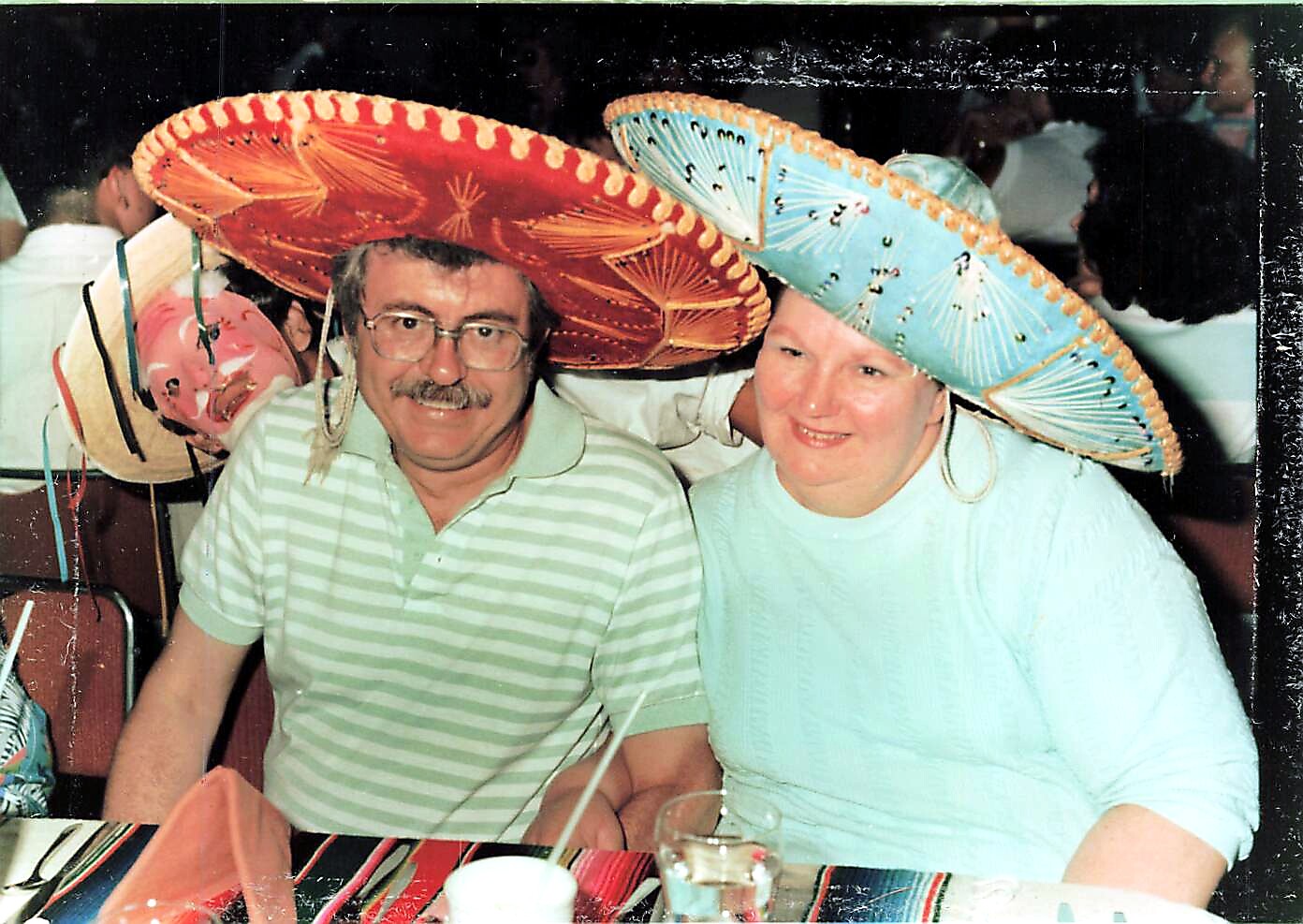 Man and woman smiling at a party, each wearing a large colorful sombrero and seated at a table.