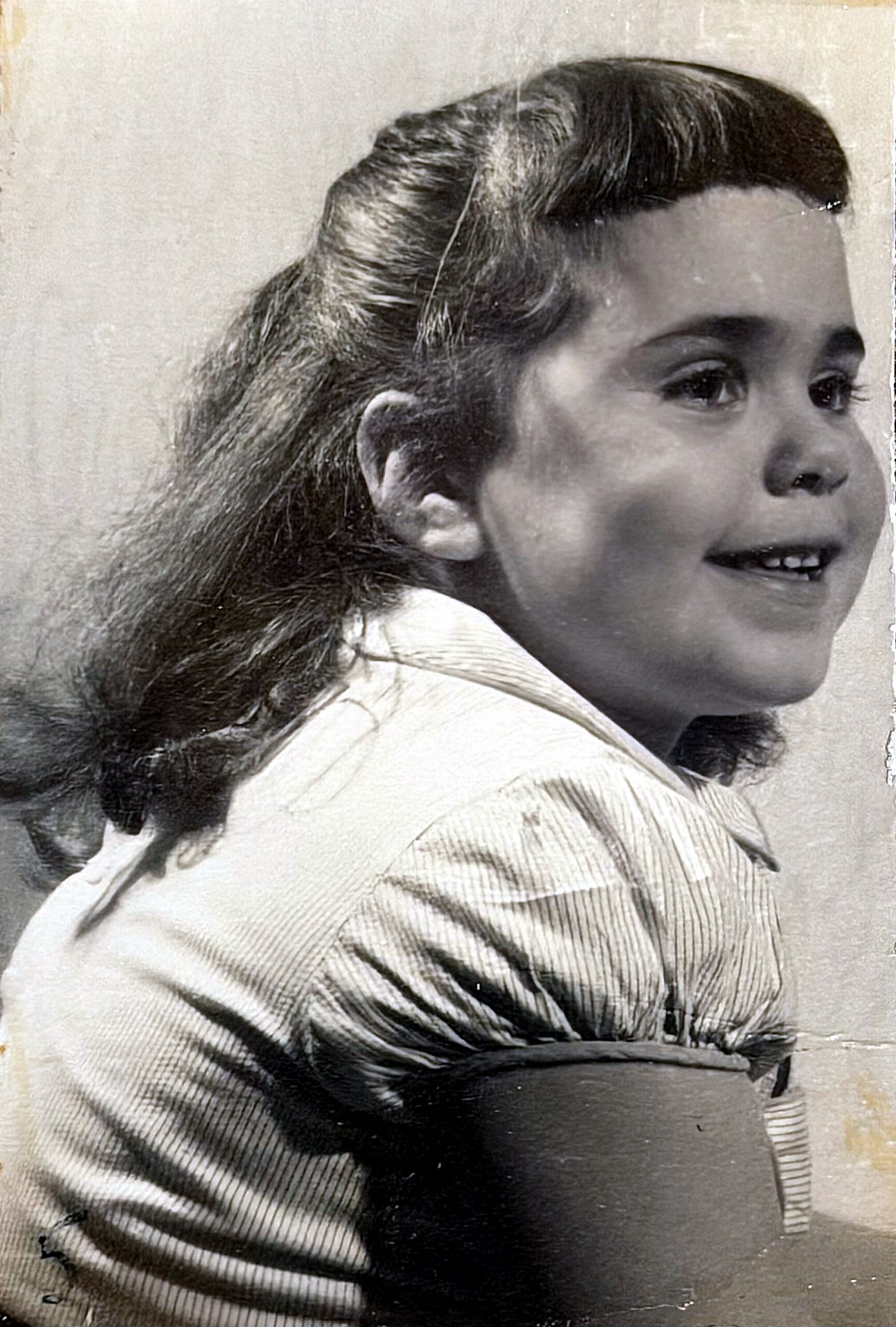 Young girl in a striped shirt smiling in a vintage black-and-white photo, side profile view with hair pulled back