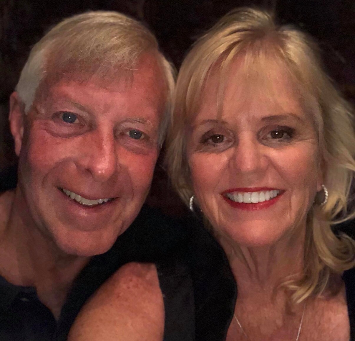 Close-up of a smiling man and woman taking a selfie together, both looking at the camera.