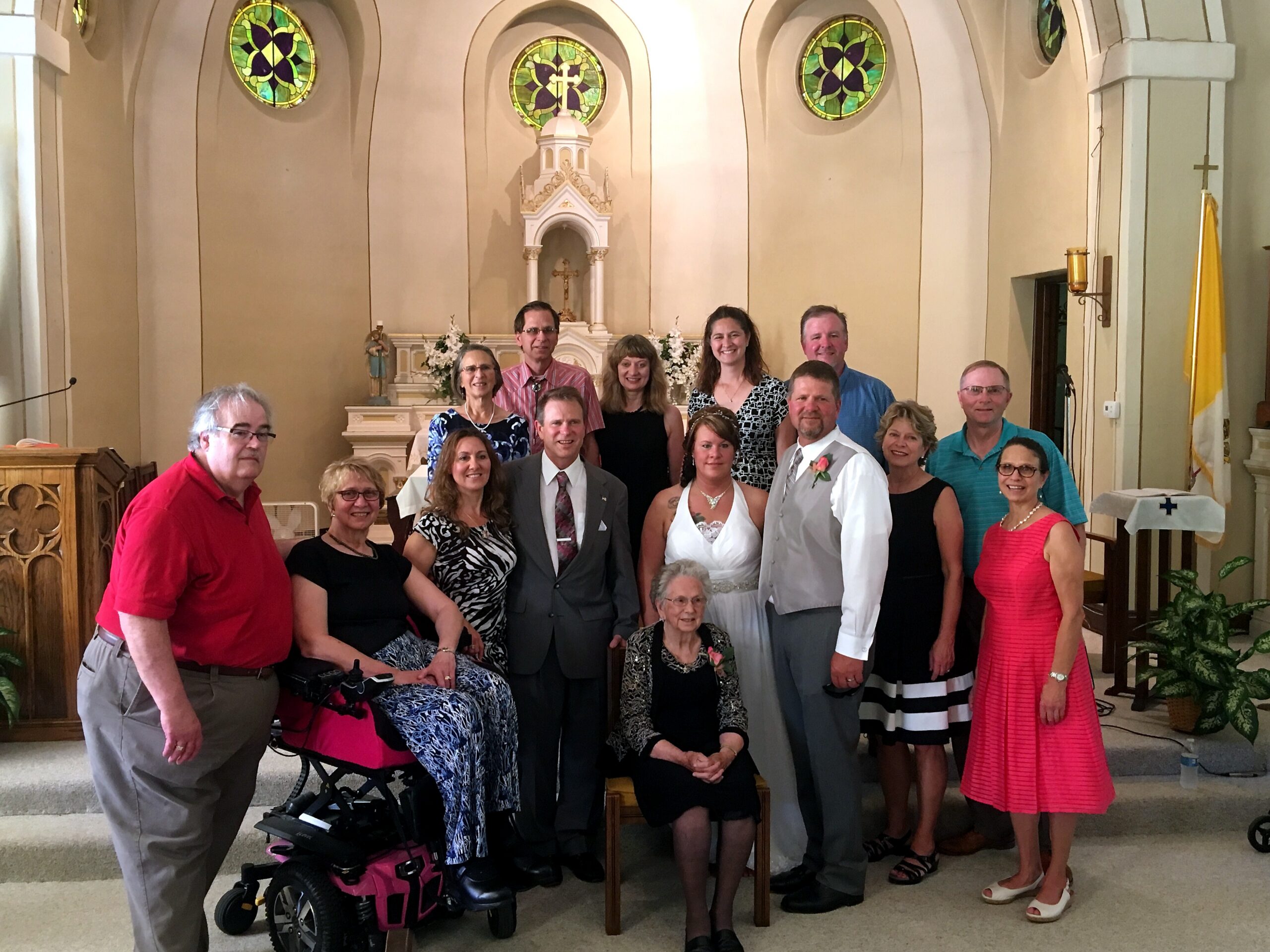 Group of people in a church sanctuary posing for a photo, with the bride and groom at the center and an ornate altar behind them.