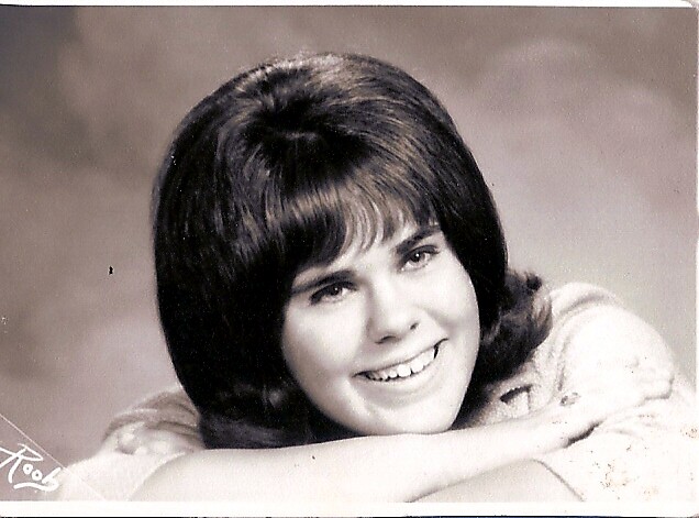 Young woman with dark hair smiles while resting her folded arms in a studio portrait.] }} |{