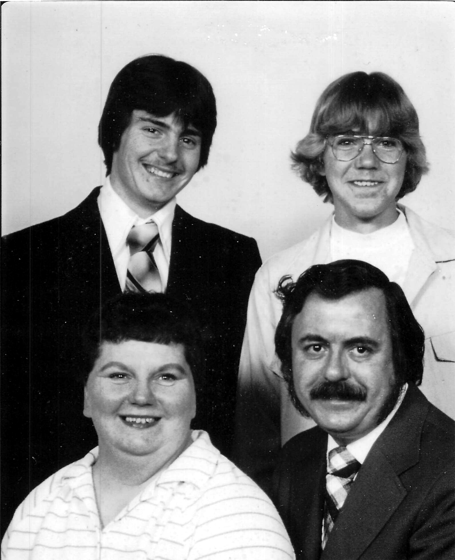 Black-and-white group portrait of four adults smiling, posed closely together in formal attire.