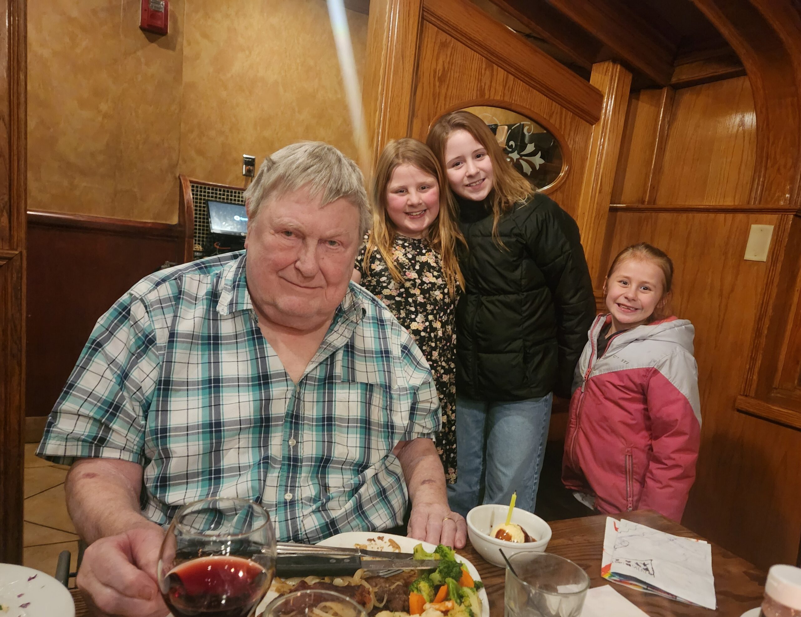 Family group at a wooden restaurant table, smiling with plates of food and drinks in front of them.