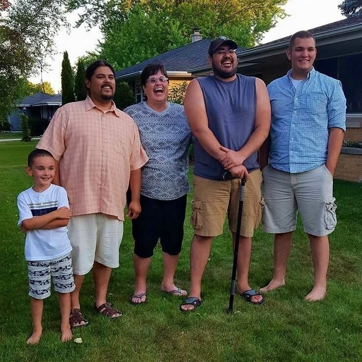 A family of six stands together on a green lawn outside a house, smiling for the photo (child in front left, adults to the right).