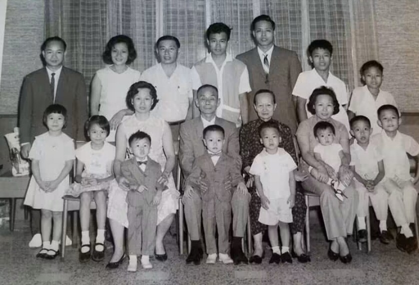 Black-and-white group portrait of a large, multi-generational family with adults, teens, and children posing in a living room.