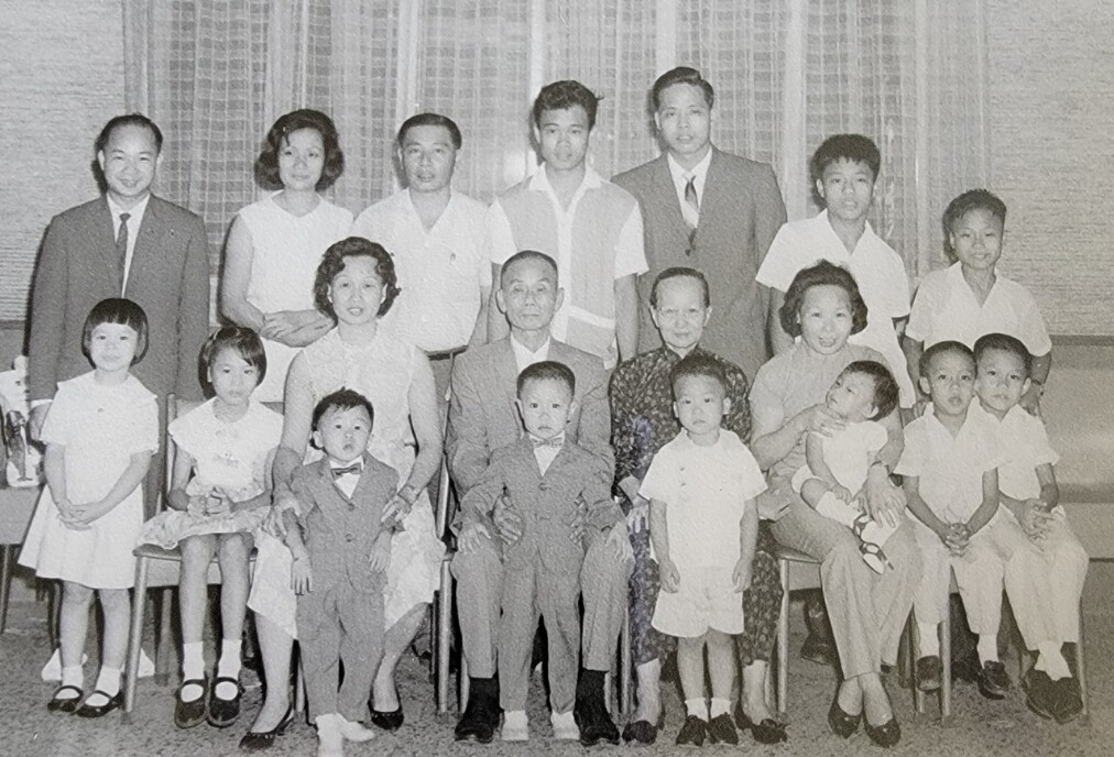 Multigenerational family portrait with grandparents seated center, parents behind, and children of various ages in front indoors.