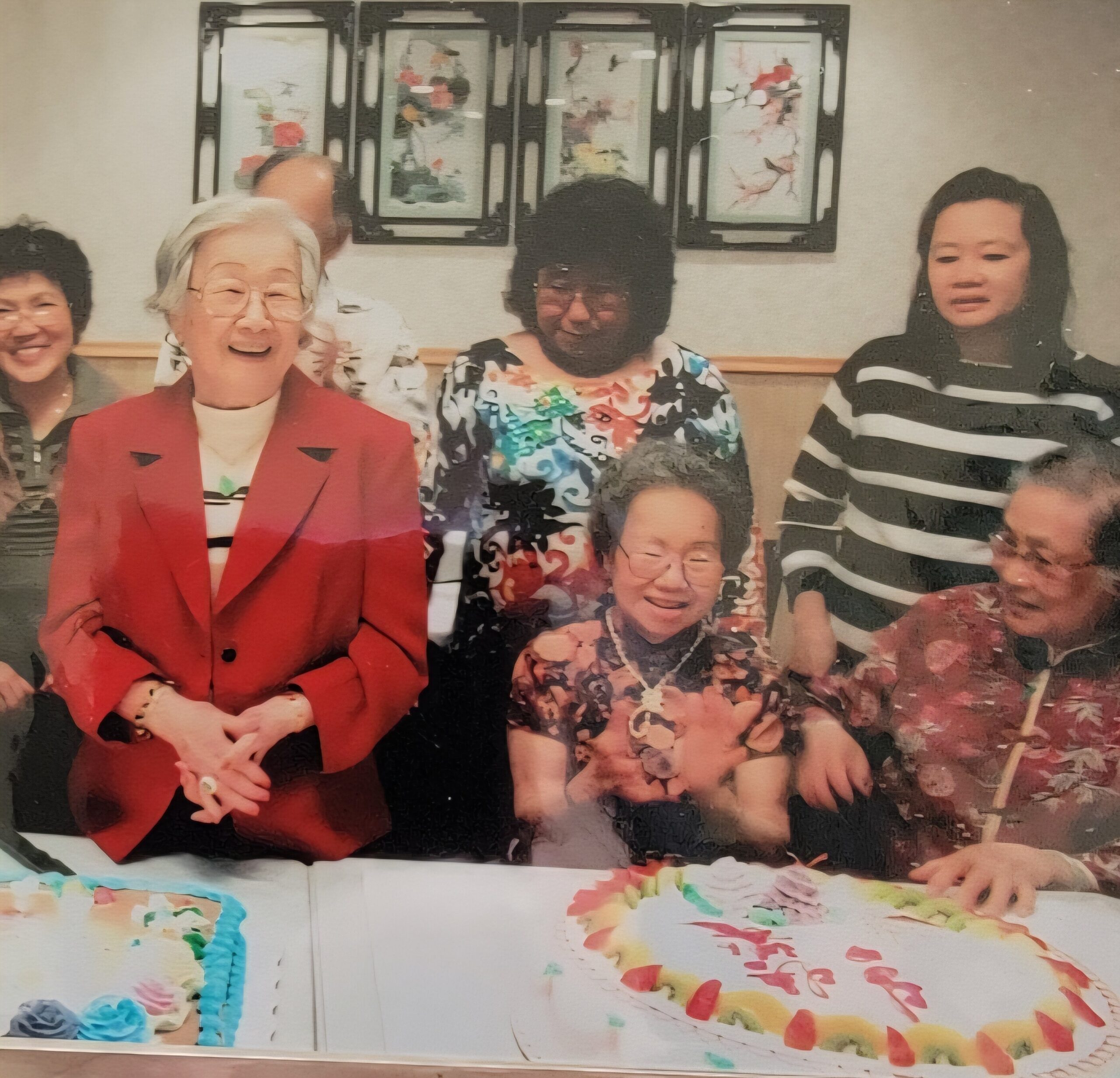 A group of people posing for a photo indoors, smiling, with colorful paper decorations on a table in front and framed wall art behind them.