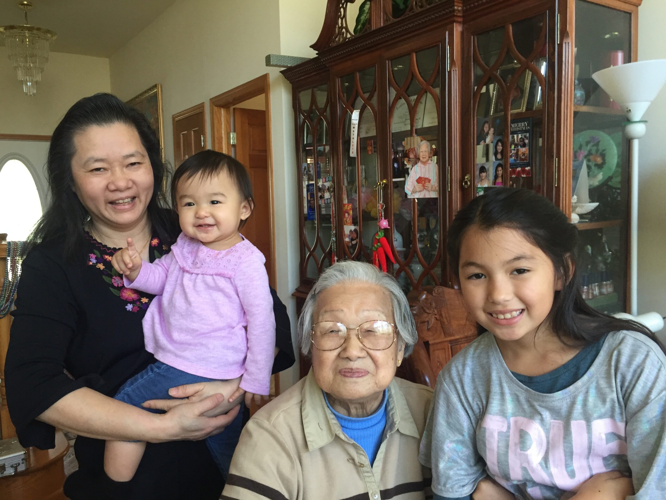 Family group posing for a photo indoors in a living room, with a wooden glass-front cabinet in the background.