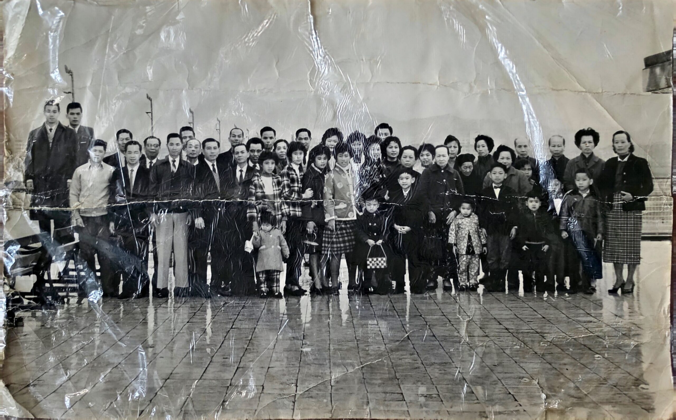Black-and-white group photo with dozens of people standing in a line indoors, including adults and children in formal and casual clothing.