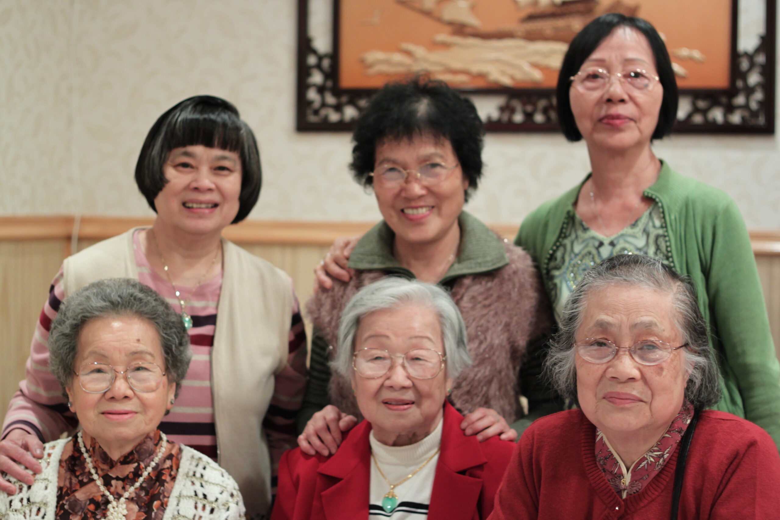 Group of elderly Asian women posing together indoors, smiling for the camera.