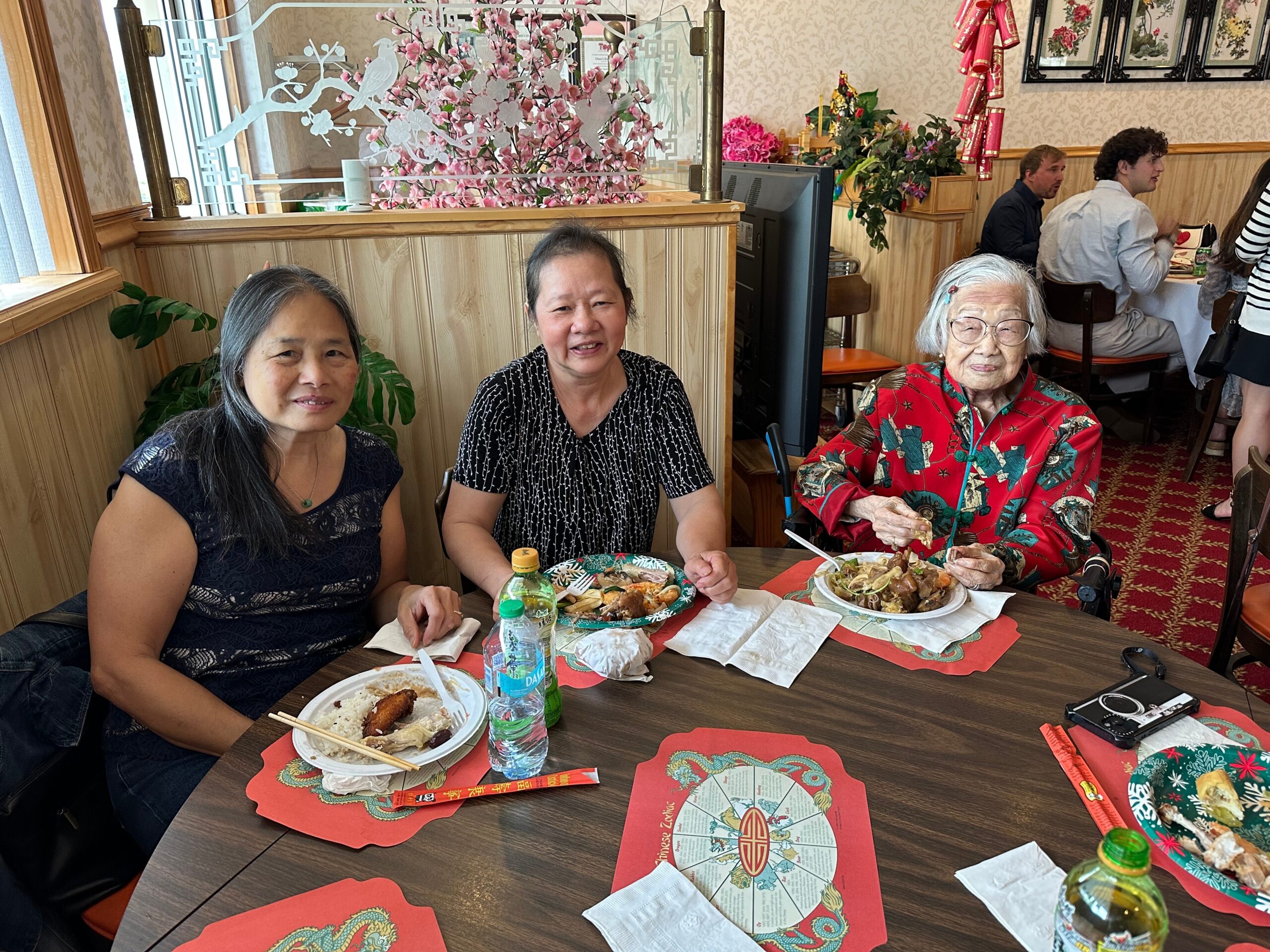 Three Asian women sit at a dining table in a restaurant, plates of food and bottles in front of them, enjoying a meal together.