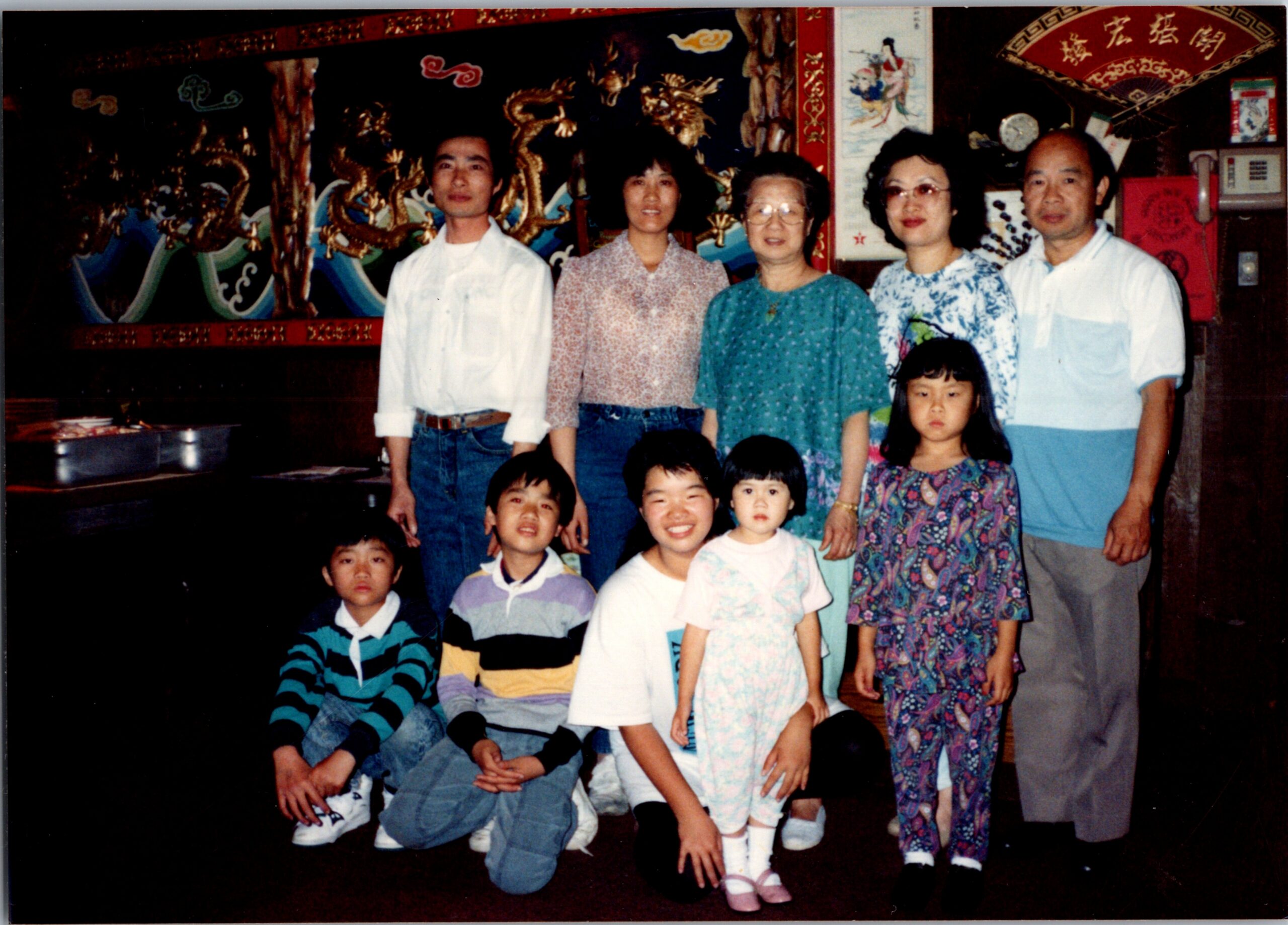 Group of adults and children posing for a casual family photo indoors, with a colorful dragon mural behind them from a cultural venue.