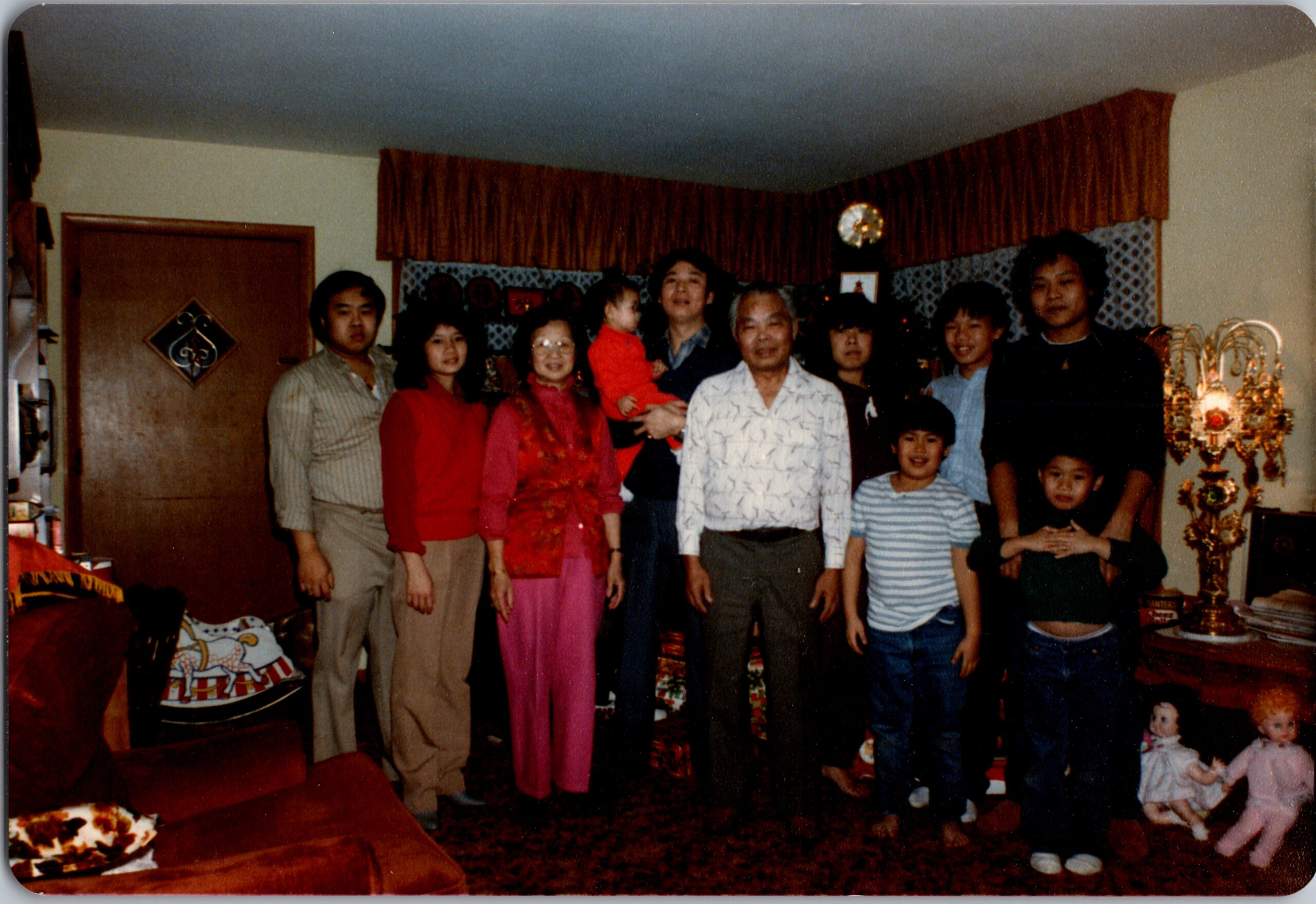 A multi‑generational family poses for a holiday photo in a living room with Christmas decorations in the background.