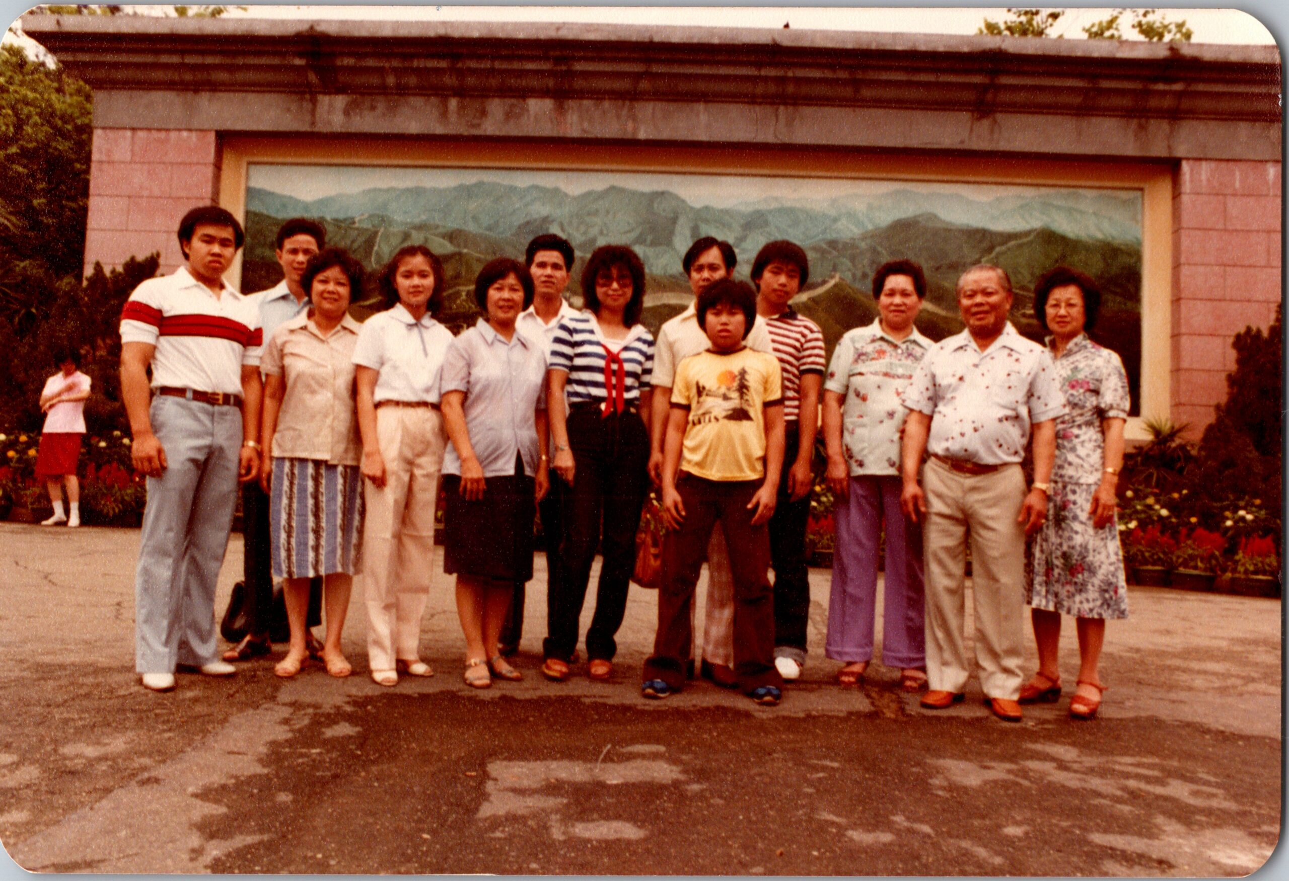 Group of adults and a child posing together outdoors in front of a large mountain mural at a park or public space.