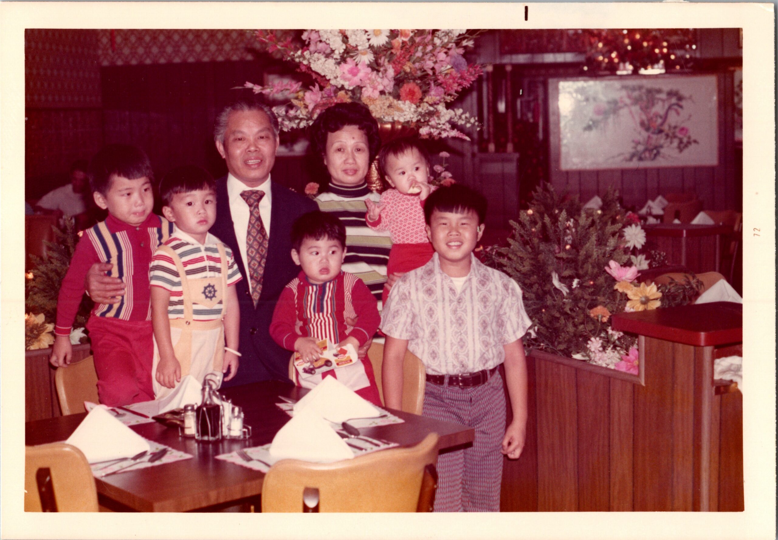 Family group photo in a restaurant with a large flower centerpiece and festive decor in the background.