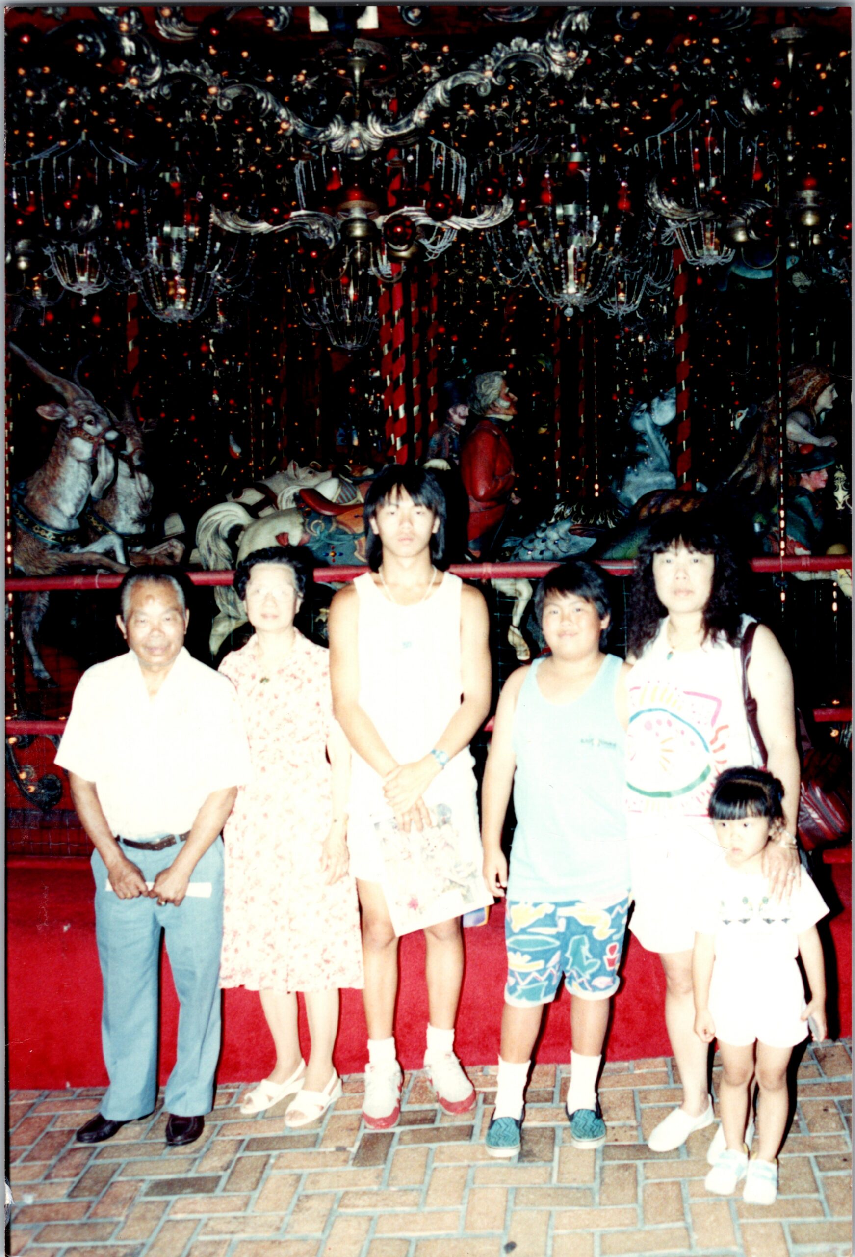 Family posing for a photo in front of a decorative carousel with carved horses and hanging lights at an amusement park.