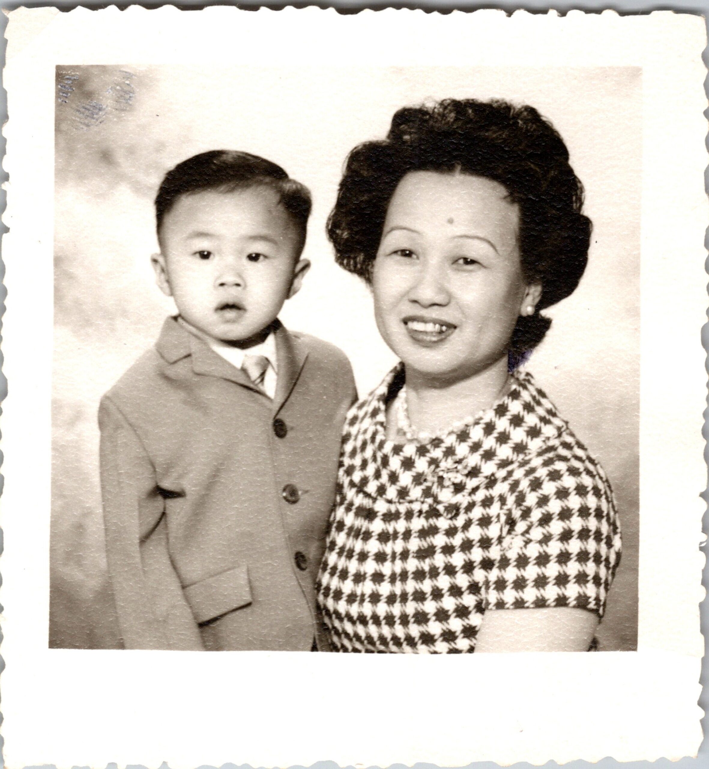 Portrait of a smiling woman with short hair posing with a young boy in a suit, both looking at the camera.
