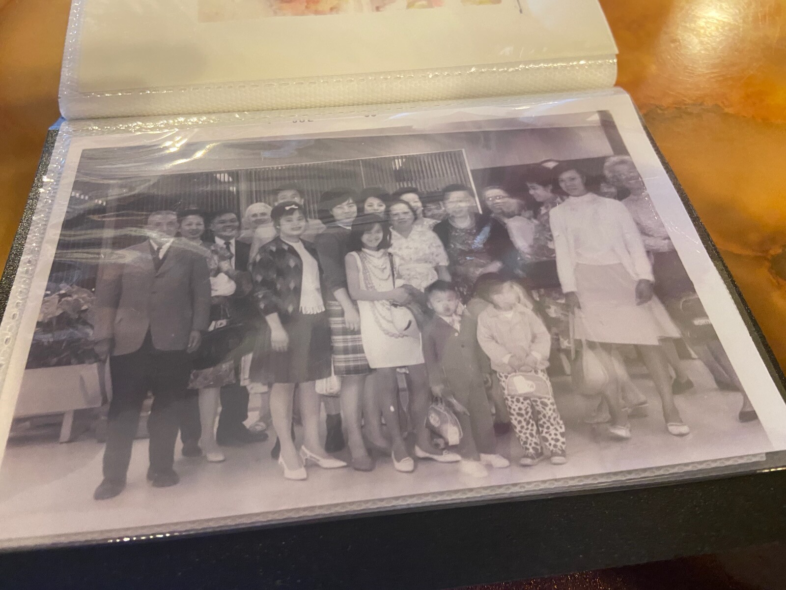 Group portrait of adults and children posing together outdoors, smiling for the camera. People wear varied clothing, suggesting a family or friend gathering.