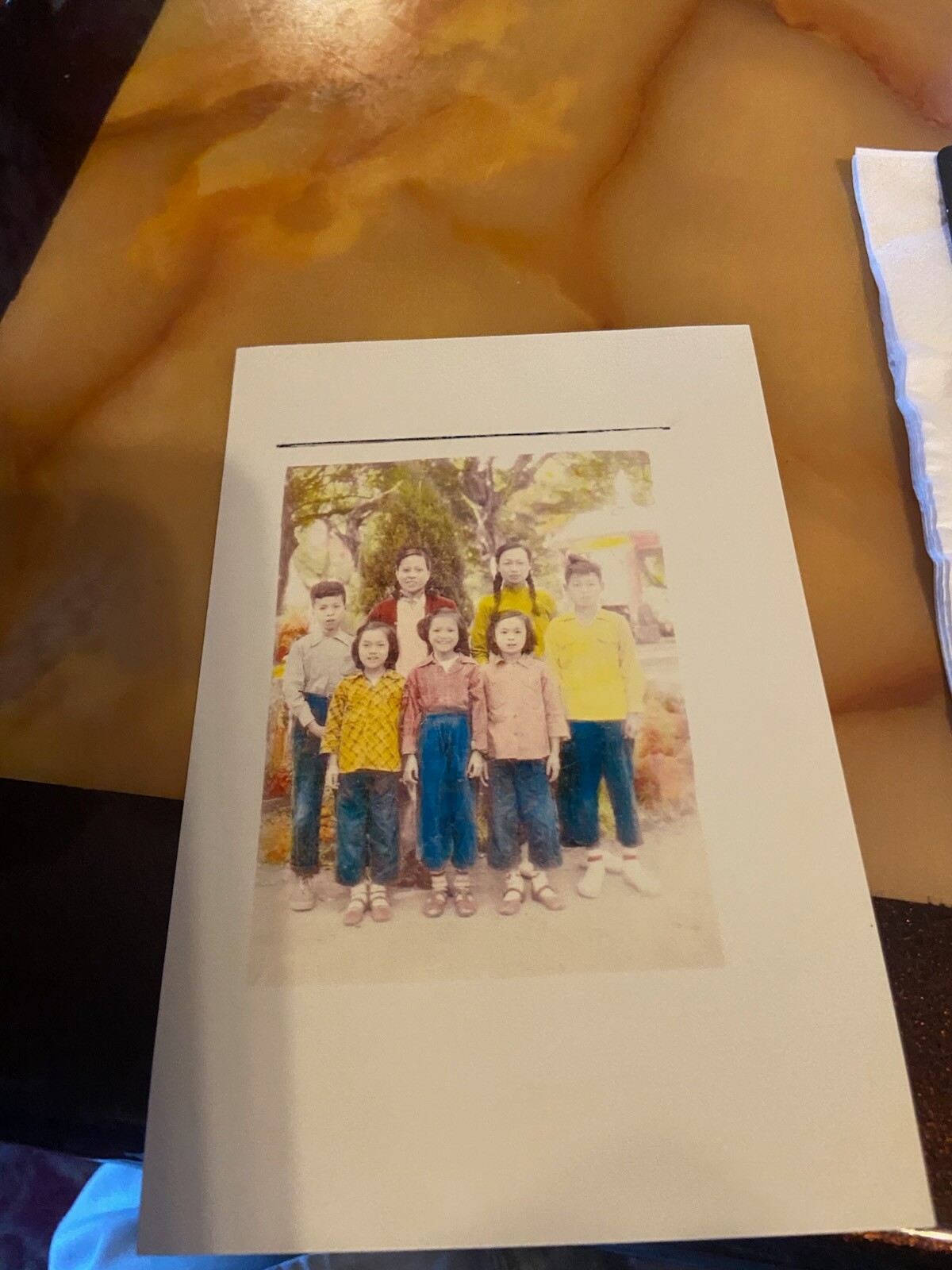 Group of children posing together outdoors in a park, standing in two rows with trees in the background.