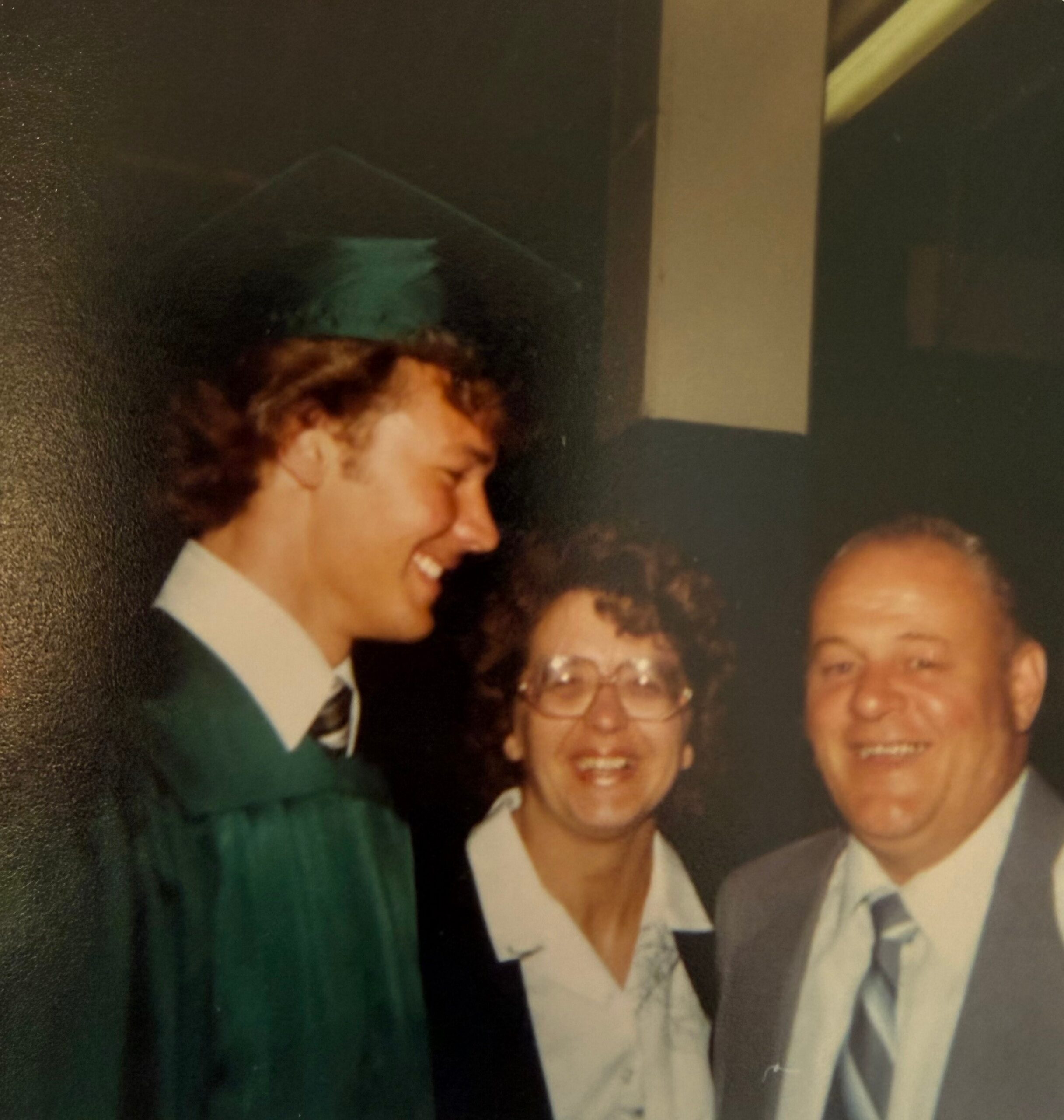 Group portrait of smiling adults at a formal event, with a man in a green suit left of center and others in light-colored jackets on the right.
