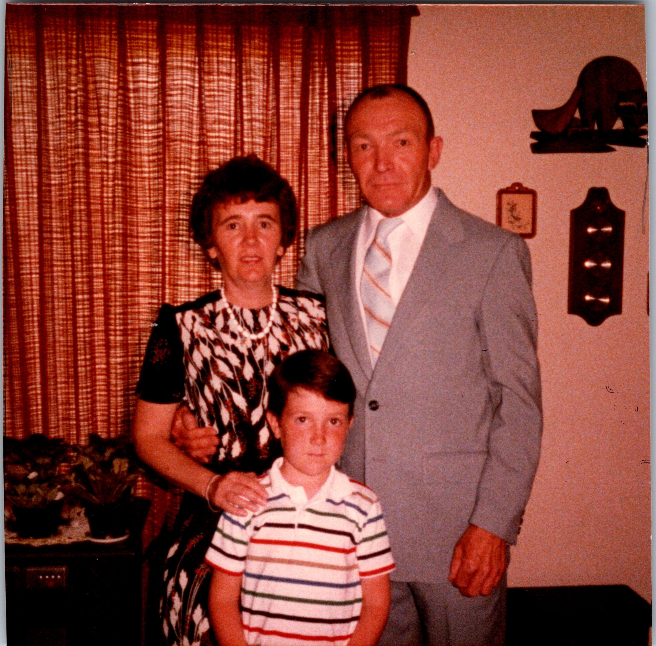 Woman and man standing with a young boy in a living room, plaid curtains in the background.