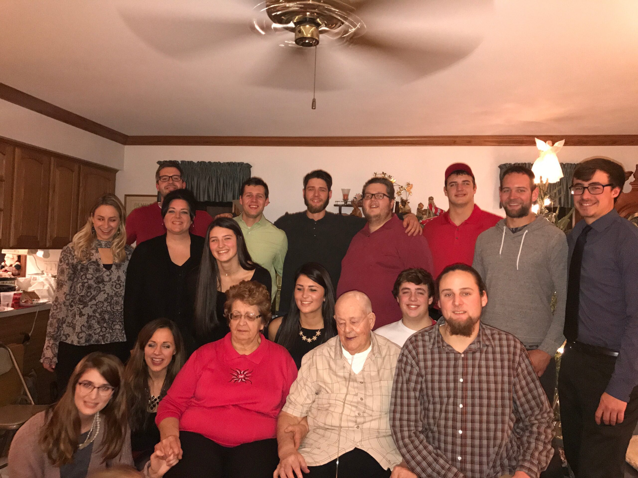 Group of people posing together for a photo in a home kitchen living area during a party or family gathering, with cabinets and decorations in the background.