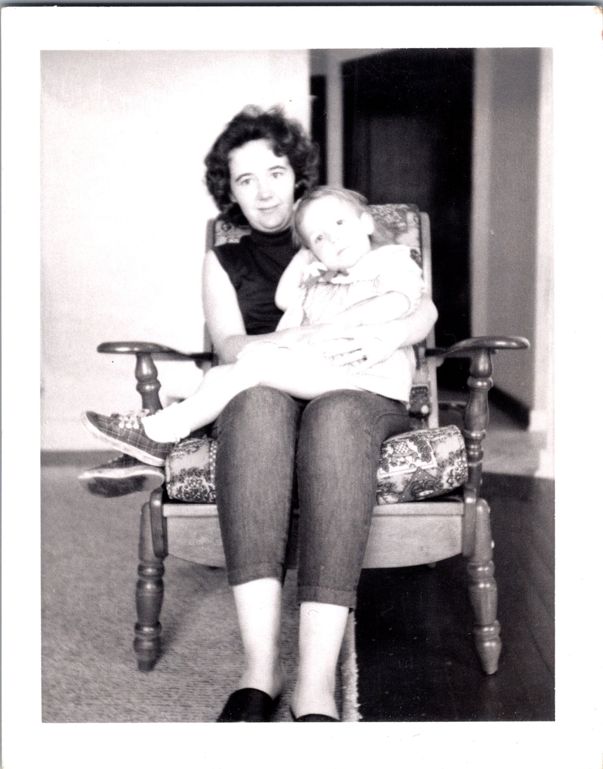 Woman smiling while holding a child on her lap in a patterned rocking chair indoors (living room).