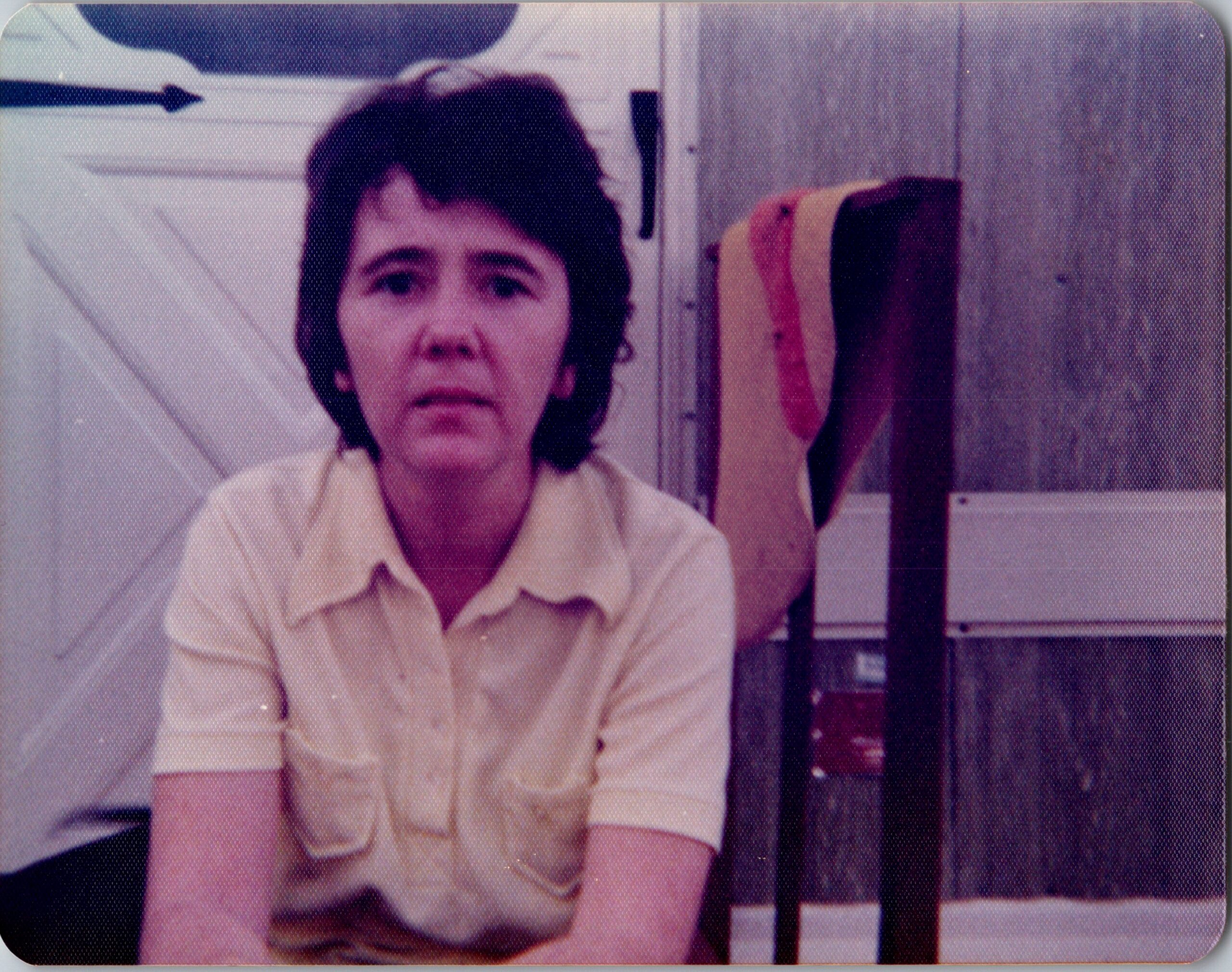 Front-facing woman with short dark hair wearing a light collared shirt, seated indoors and looking at the camera.