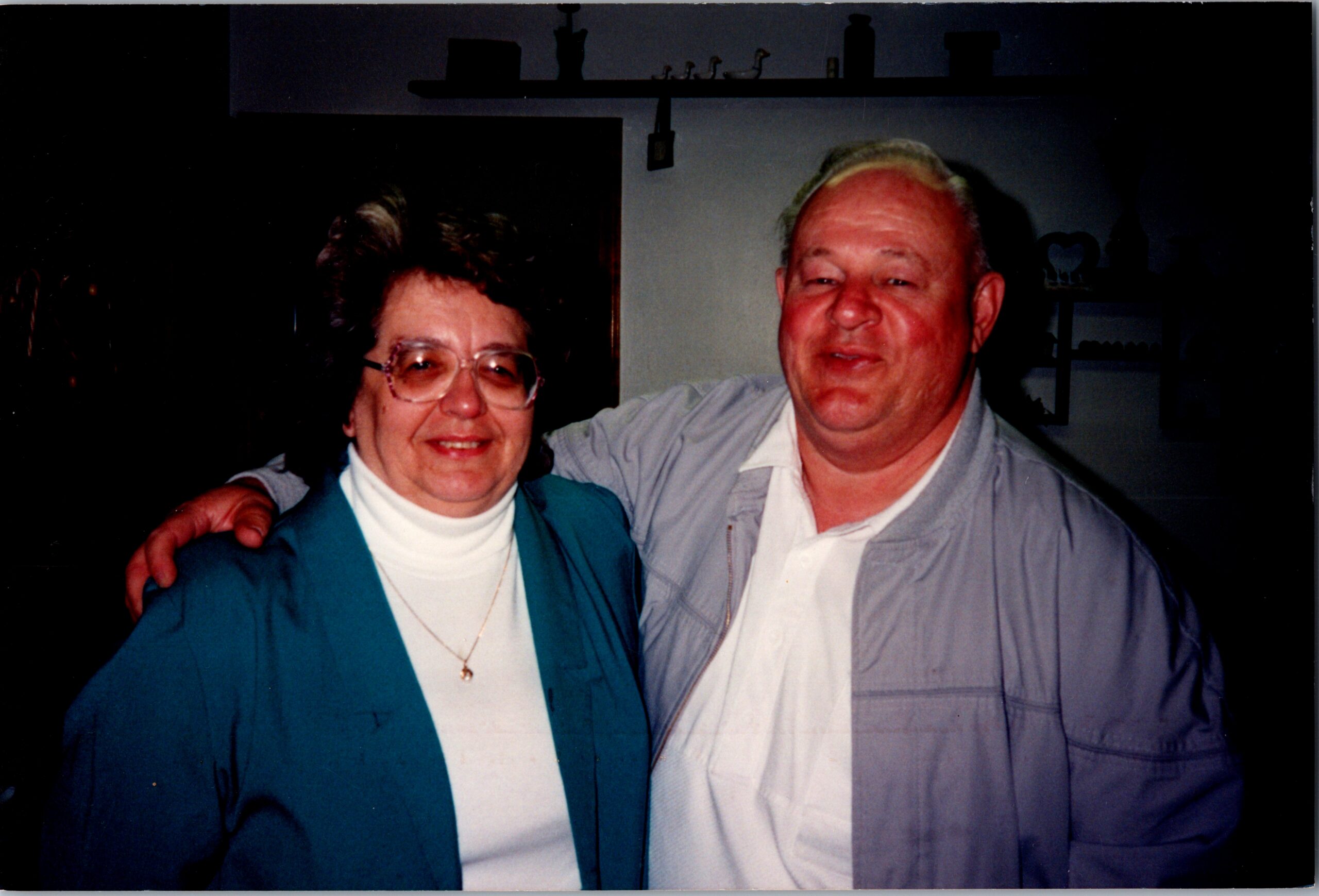 Smiling elderly couple with arms around each other indoors, posing for a photo.