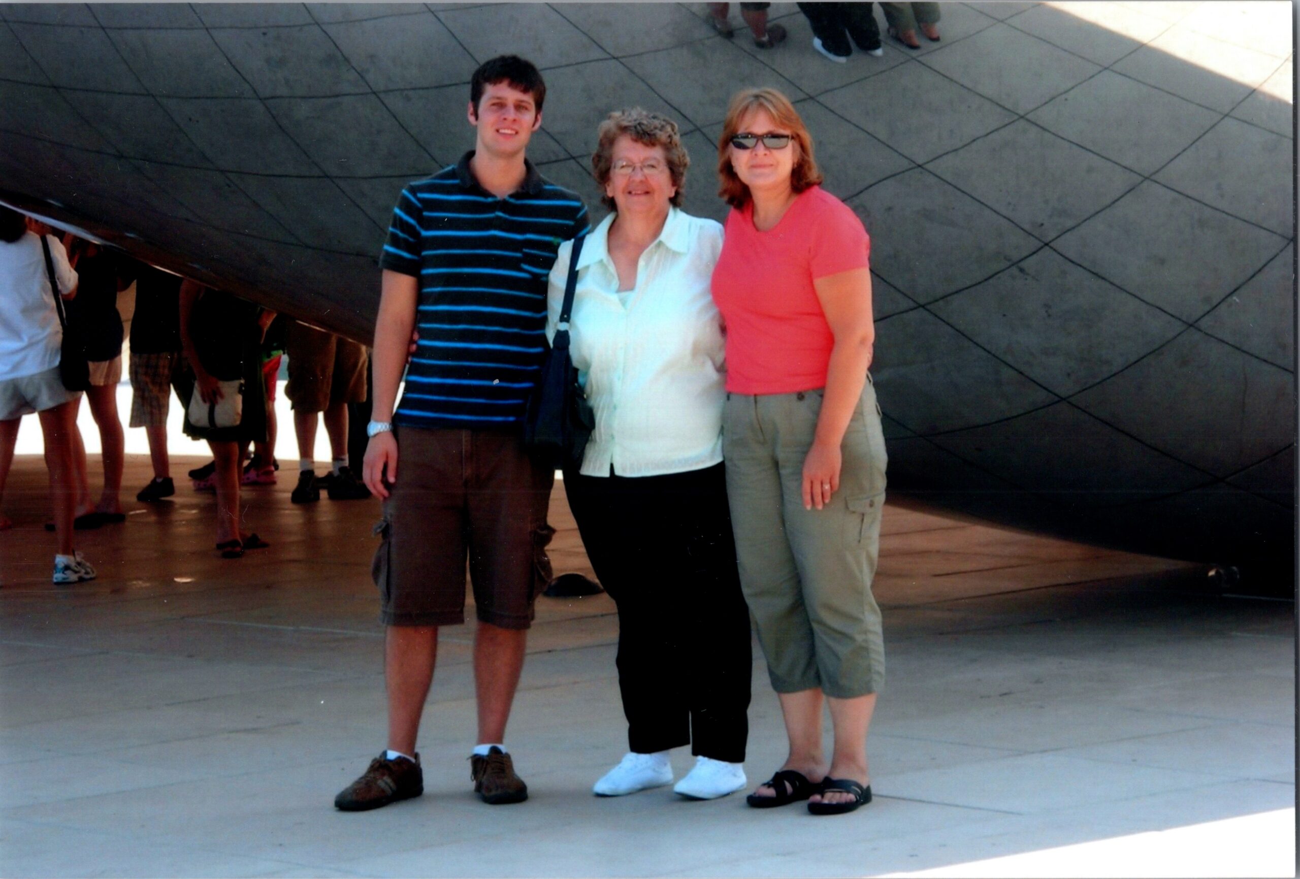 Three people posing outdoors in front of a large curved reflective wall, smiling for the camera (man on left, two women in middle and right).