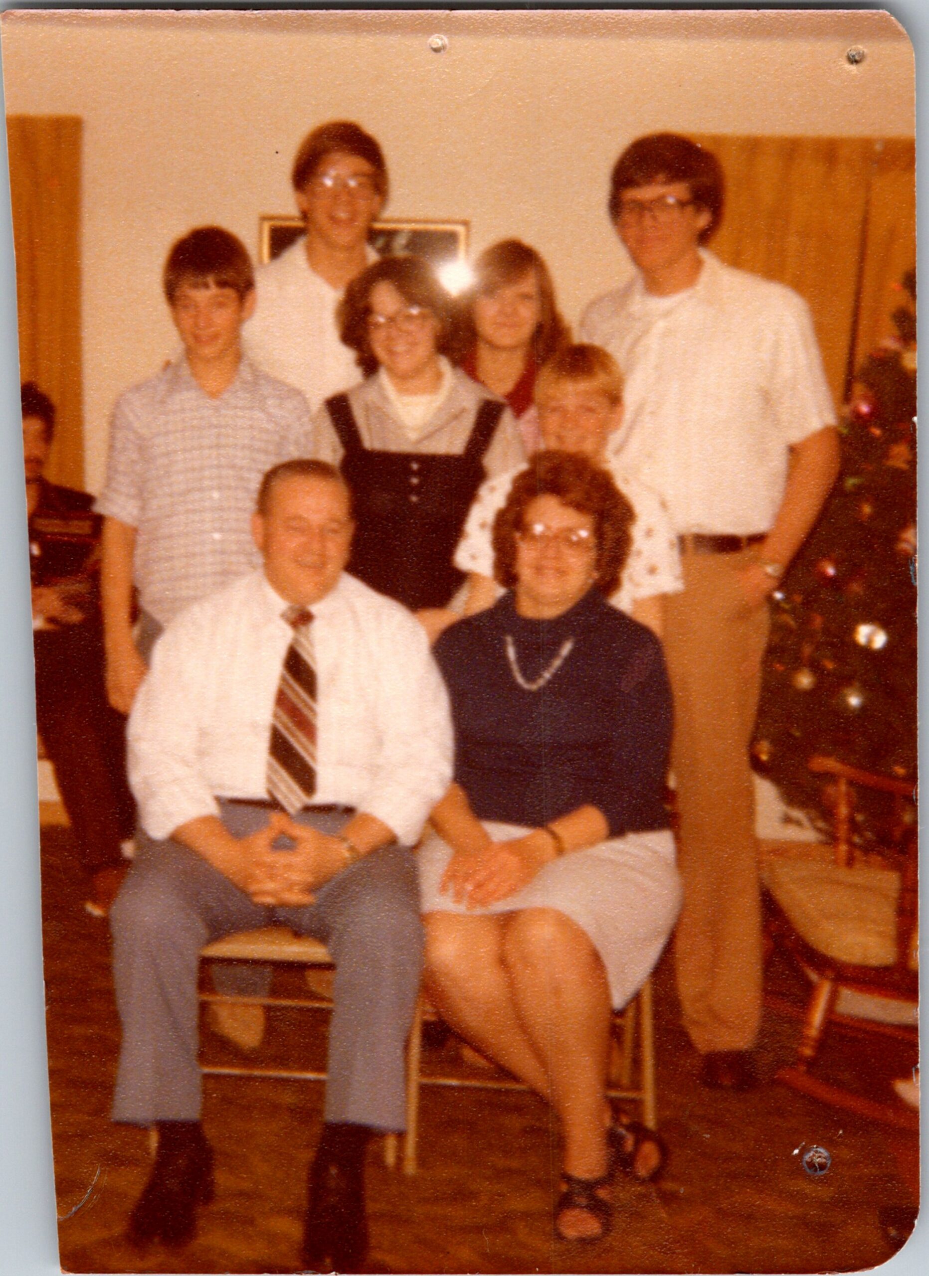 A multi-person family group posing for a photo indoors, with several adults standing behind two people seated in a living room.